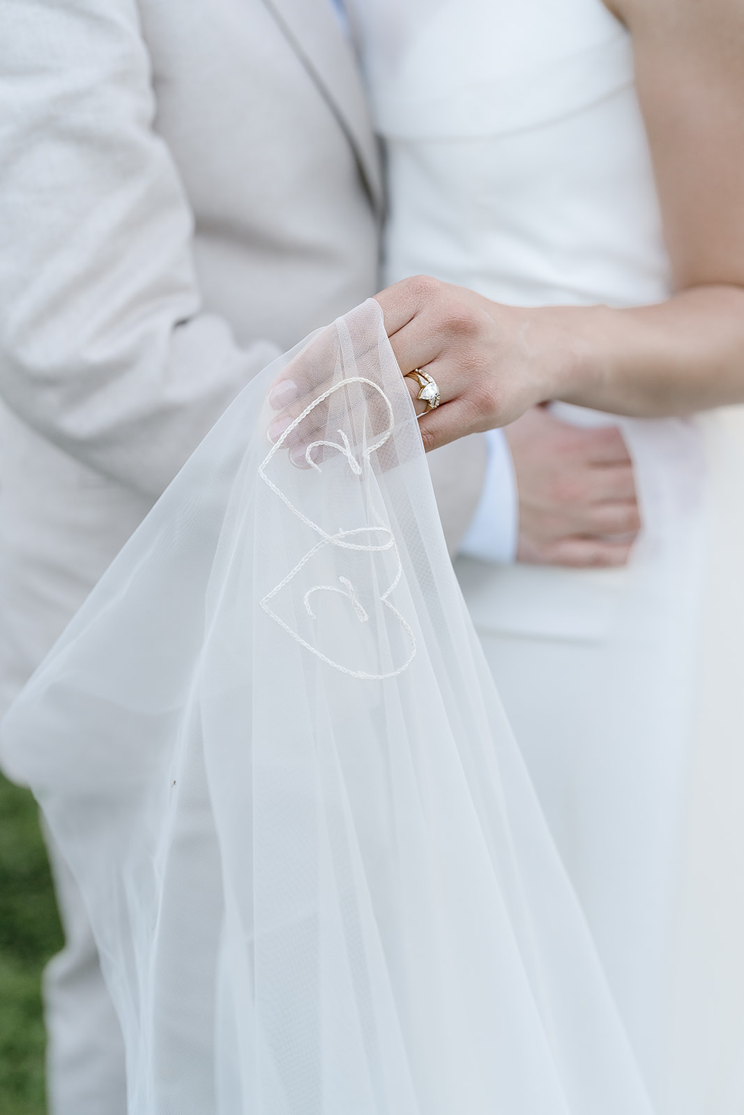 A couple embraces with the bride holding her veil. The veil has two embroidered hearts and the initials "J" and "C.