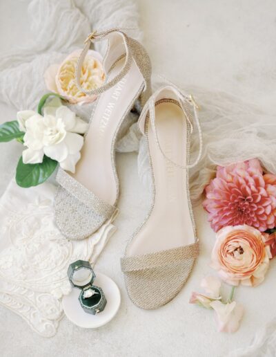 Sparkly high-heeled sandals with floral accents, lace fabric, and two small jewelry boxes on a light background.