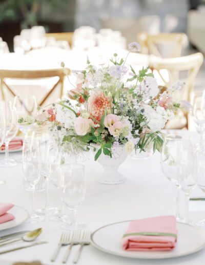 A floral centerpiece with pink and white flowers on a table set with plates, pink napkins, glassware, and cutlery.