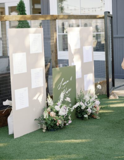 Seating charts and a welcome sign with floral arrangements are displayed on a lawn.