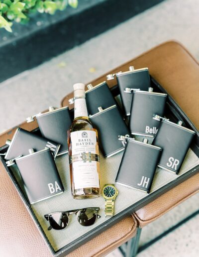 A tray with multiple black flasks, a bottle of Basil Hayden's bourbon, a wristwatch, and sunglasses.