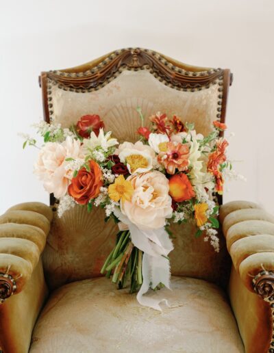 A bouquet of colorful flowers, including roses and daisies, is placed on an ornate vintage chair with a velvet cushion.