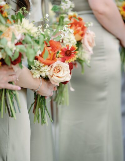 Bridesmaids in green dresses holding bouquets of orange, white, and yellow flowers.