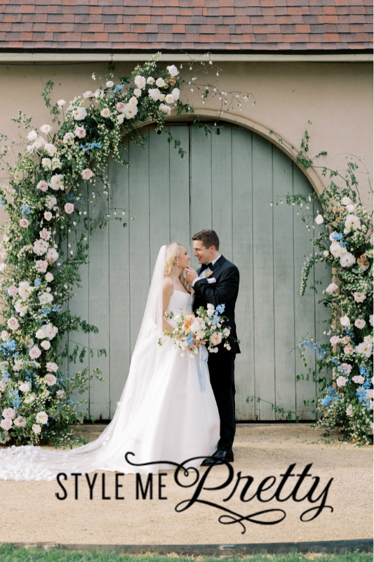 Bride and groom stand in front of a floral arch, holding hands and gazing at each other. The ground is lined with pink flowers, a testament to the impeccable touch of Tahoe wedding planners.