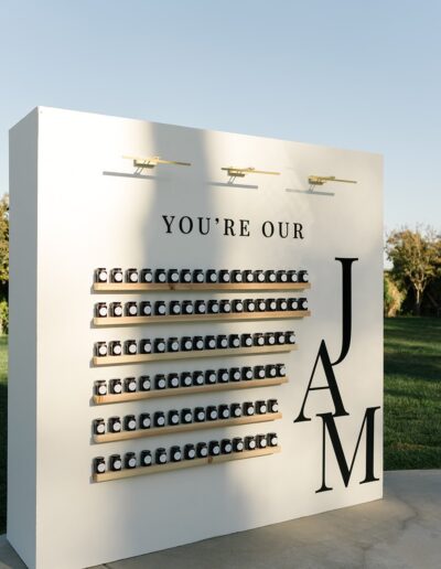 Display board with small jars arranged neatly, featuring the text "You're Our Jam" and a large letter "JAM" on the right side, set outdoors in sunny weather.