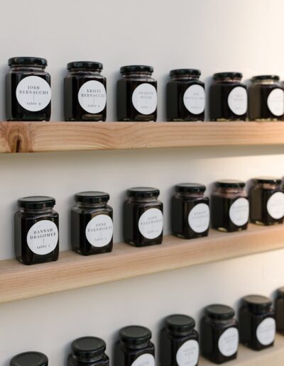 Jars with name labels on wooden shelves, arranged in rows against a plain wall.