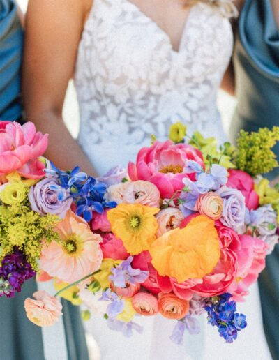 In a white lace dress, a person gracefully holds a vibrant bouquet filled with colorful blooms in pink, yellow, and purple—perfectly capturing the romance of a Napa Valley wedding.