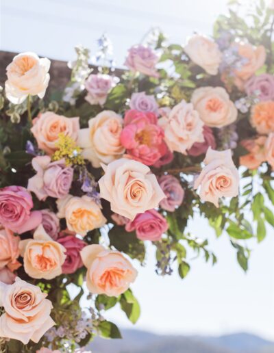 A colorful floral arrangement with pink, peach, and lavender roses graces the scene, reminiscent of a vibrant Napa Valley wedding beneath a bright, sunny sky.