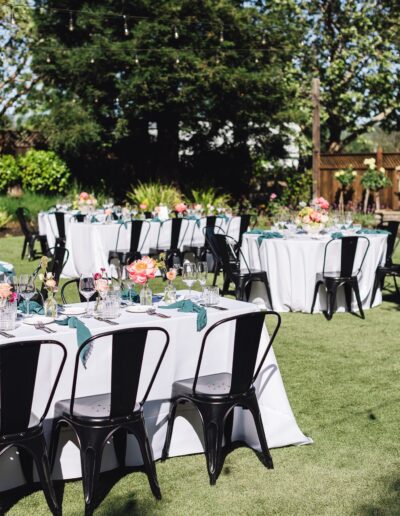 Outdoor dining setup with round tables draped in white cloths, black chairs, and floral centerpieces on a grassy lawn, perfect for a Napa Valley wedding.