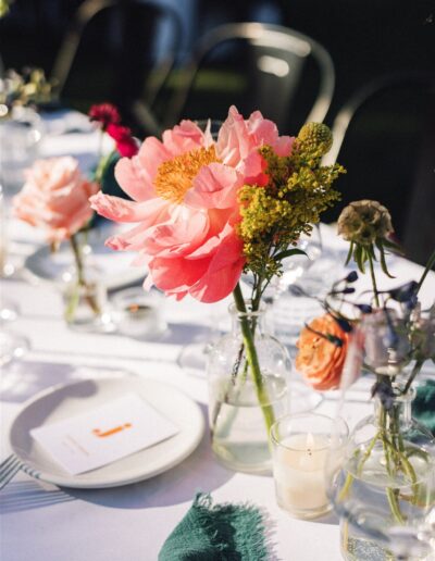 A table set for a Napa Valley wedding features a white tablecloth, elegant place settings, and glass vases filled with bright pink and yellow flowers.