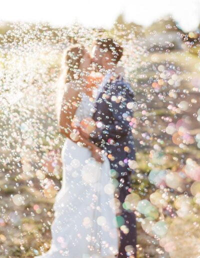 A couple stands close together in the dreamy outdoors of a Napa Valley wedding, surrounded by a shower of bubbles.