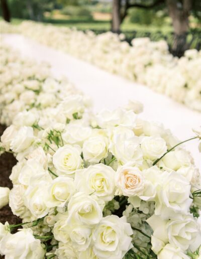 A pathway lined with abundant white roses, leading through a garden setting.