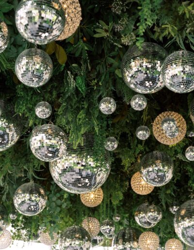 A ceiling decorated with mirrors, greenery, and round, silver reflective disco balls mixed with clusters of small golden lights.