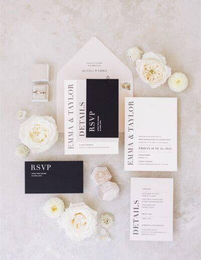 Flat lay of black and white wedding stationery set with RSVP cards, invitation, and details card. Surrounded by white flowers and an open envelope.