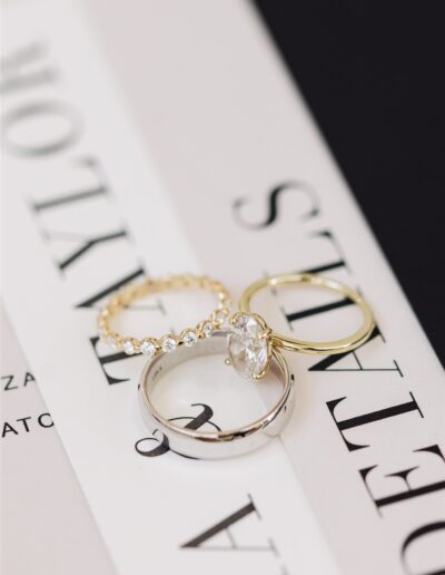 Three rings displayed on a book cover: a gold band with stones, a plain gold band, and a silver band with a large stone.