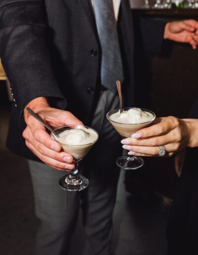 Two people holding martini glasses with a creamy dessert, dressed in formal attire.