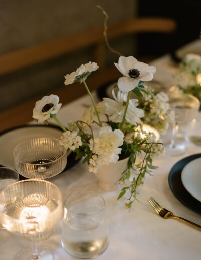 Elegant table setting with white flowers in a vase, surrounded by glassware and plates on a white tablecloth.