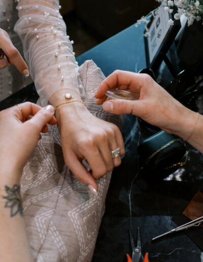 Person assisting another with a bracelet at a table, with a cocktail and tools nearby.