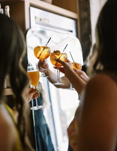 Four people clinking glasses filled with orange drinks in a celebratory toast near a mirror.