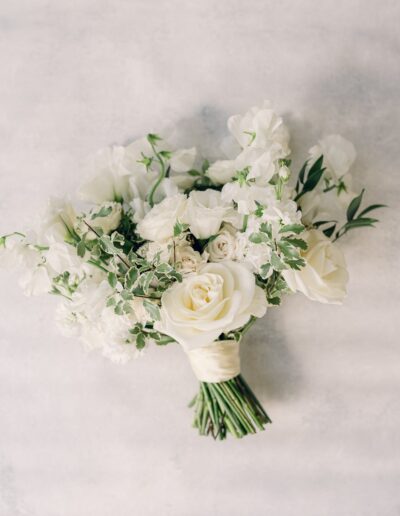 A bouquet of white roses and greenery against a light background.