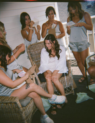 A group of women in casual attire sit and stand on a porch, sharing a light moment and exchanging cards or notes.