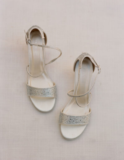 A pair of beige high-heeled sandals with ankle straps and textured front bands placed on a neutral surface.