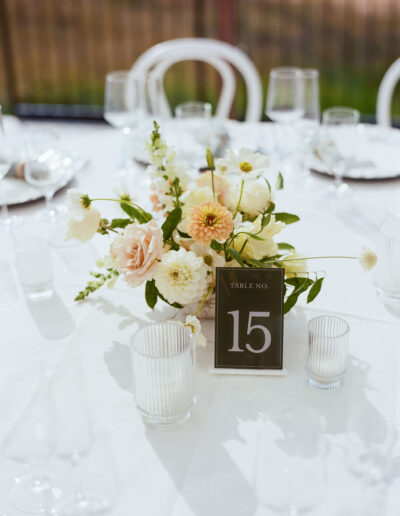 A table setting with a floral centerpiece and a card displaying "Table No. 15," surrounded by empty glasses and plates on a white tablecloth.