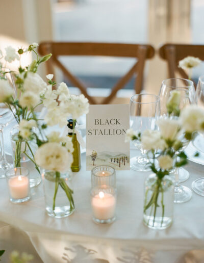 Elegant table setting with white flowers in vases, lit candles, wine glasses, and a card reading "Black Stallion.