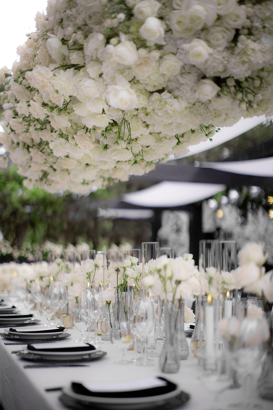 Elegant dining table with white floral centerpiece, black plates, clear glassware, and white napkins.