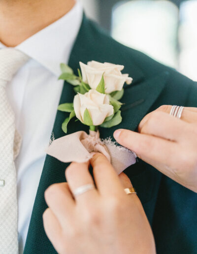 A person adjusts a boutonniere with pale roses on a suit jacket.