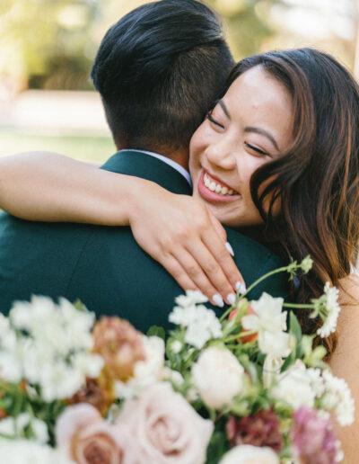 A smiling woman embraces a man outdoors, holding a bouquet of assorted flowers.