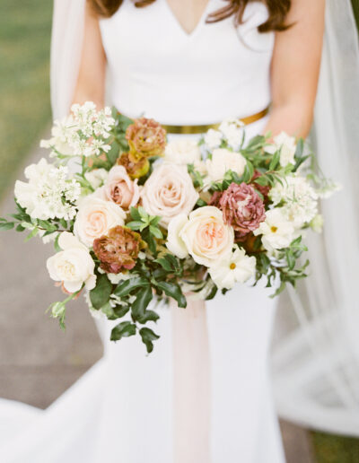 A bride in a white dress holds a bouquet with pink, white, and beige flowers.