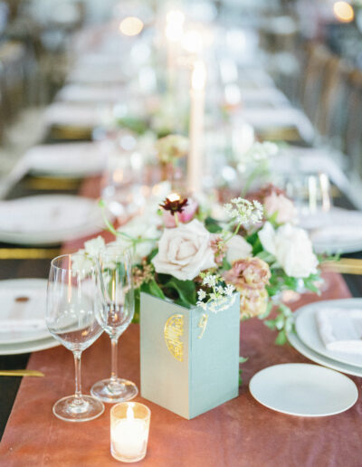 Elegant table setting with floral centerpiece, wine glasses, plates, and lit candles on a long table with a pink table cloth.