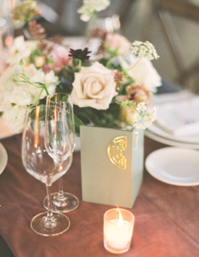 A table setting with a floral arrangement in a box, two empty wine glasses, a small lit candle, and a white plate.