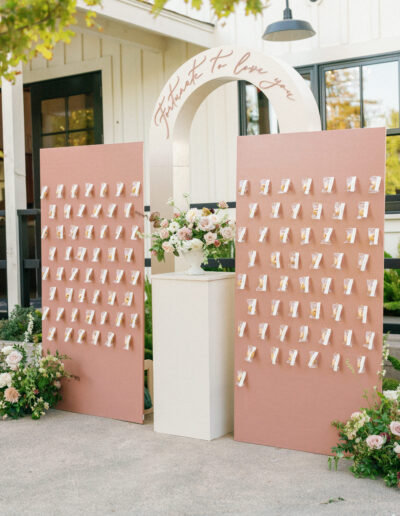 Wedding seating chart display with two pink boards featuring guest name cards, floral arrangements, and an arch with "It Was Fate To Love You" written above.