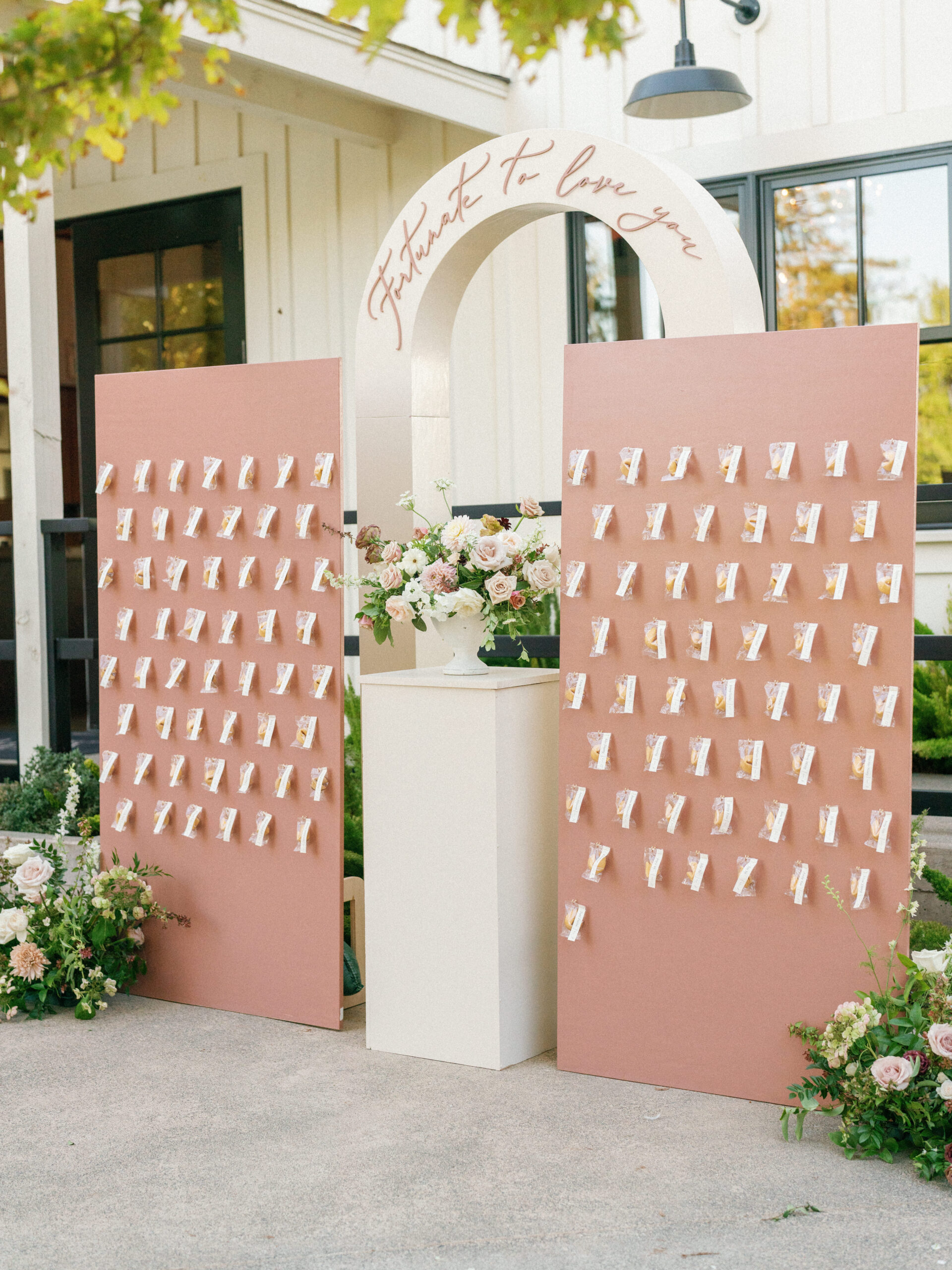 Wedding seating chart display with two pink boards featuring guest name cards, floral arrangements, and an arch with "It Was Fate To Love You" written above.