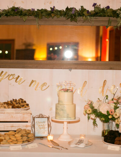 A dessert table with a cake, various cookies, and photos in frames. A sign reads "you, me and dessert" and there are flowers and small lit candles for decoration.