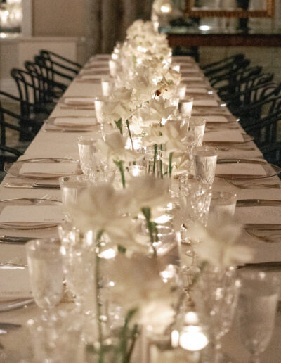 A long dining table is elegantly set with white floral centerpieces, candles, glassware, and silverware.