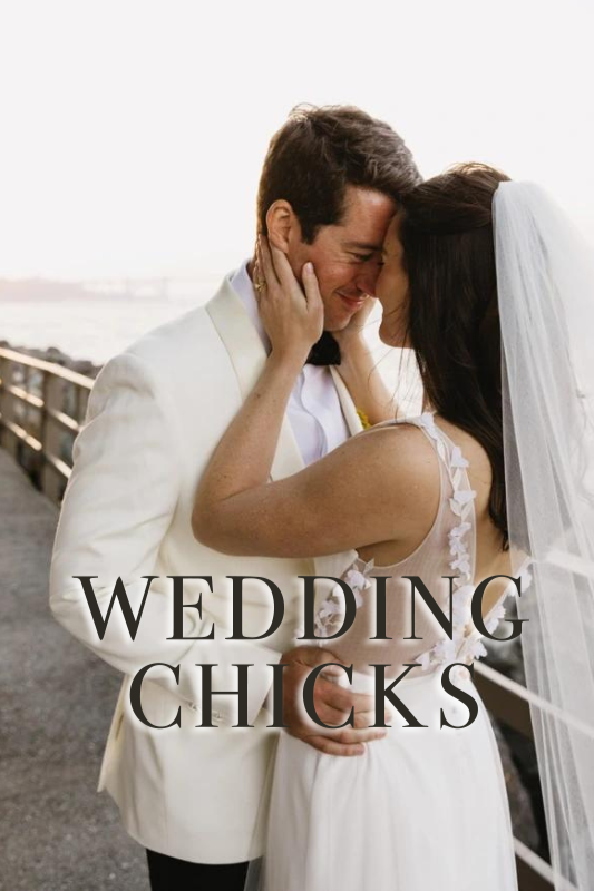 A bride and groom embrace and smile at each other on a waterfront boardwalk, with the text "Wedding Chicks" overlaid on the image.