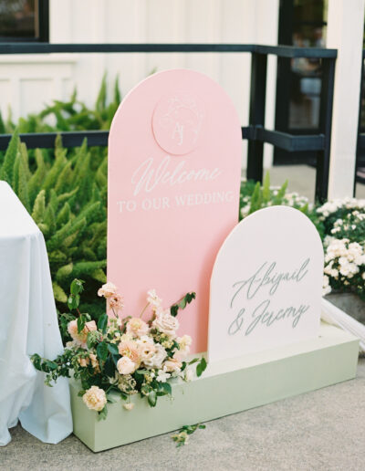 Wedding welcome signs reading "Welcome to Our Wedding" and "Abigail & Jeremy" with flower decorations, displayed outdoors.