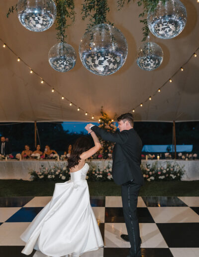 A couple dances under disco balls on a black and white checkered floor at an outdoor event.