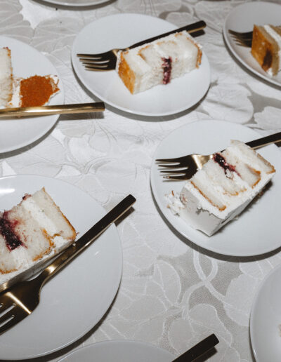 Slices of layered cake with white frosting and a berry filling are served on white plates with forks on a table.