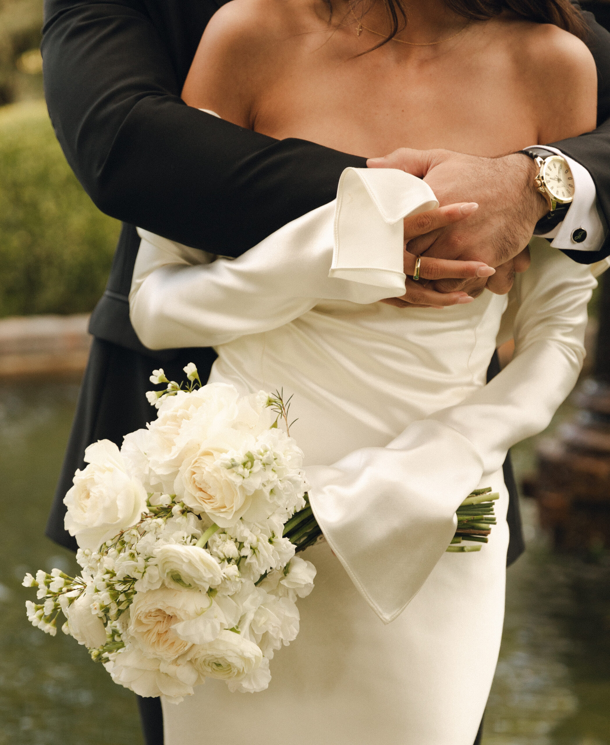 A person in a white dress holds a bouquet of white flowers while being embraced by someone in a black suit.