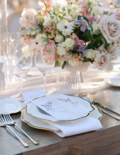 A table setting with floral centerpiece, elegant dinnerware, glassware, and a menu card placed on a wooden surface.