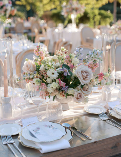 Elegant table setting with floral centerpiece, glassware, and tableware on a wooden table outdoors.