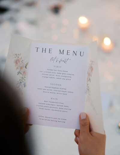 Person holding a menu with floral design, listing courses such as yellowtail tuna salad, seared scallop, and kingfish with dessert options mentioned.