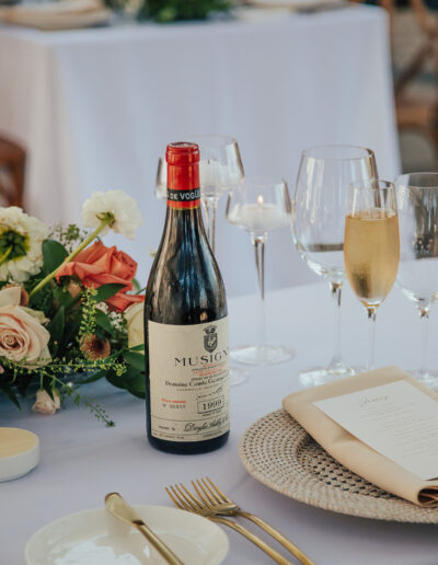 A bottle of wine is on a table set with flowers, wine glasses, a champagne flute, and a menu.