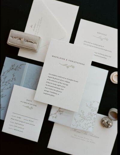 A set of elegant wedding invitations and RSVP cards arranged on a dark surface, accompanied by a ring box and decorative envelopes.