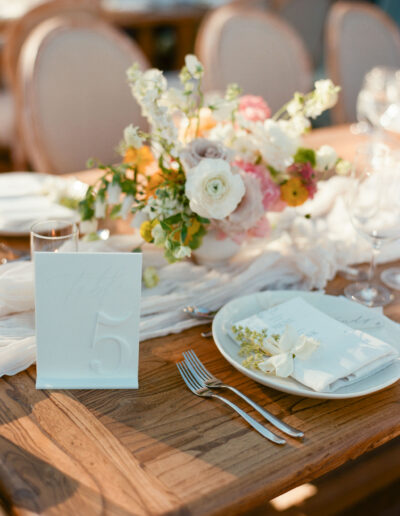 Table setting with a floral centerpiece, a plate with a napkin and small flowers, and a table number card.