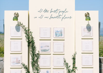 Elegant seating chart display with yellow panels, floral arrangements, and calligraphy reading "all the best people in all our favorite places." Cards are arranged in a grid.